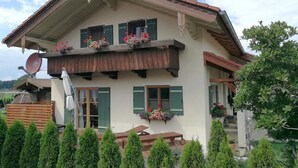 A two-story house with a balcony, green shutters, and flower boxes. - Ferienwohnung bis 2 Personen, Erdgeschoss, Terrasse (Grassau)