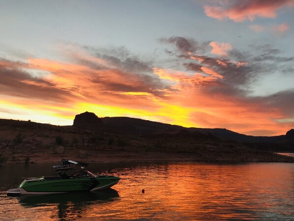 A boat on calm water with a sunset and mountains in the background.