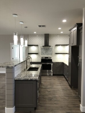 A modern kitchen with a central island, stainless steel appliances, and a white-tiled backsplash.
