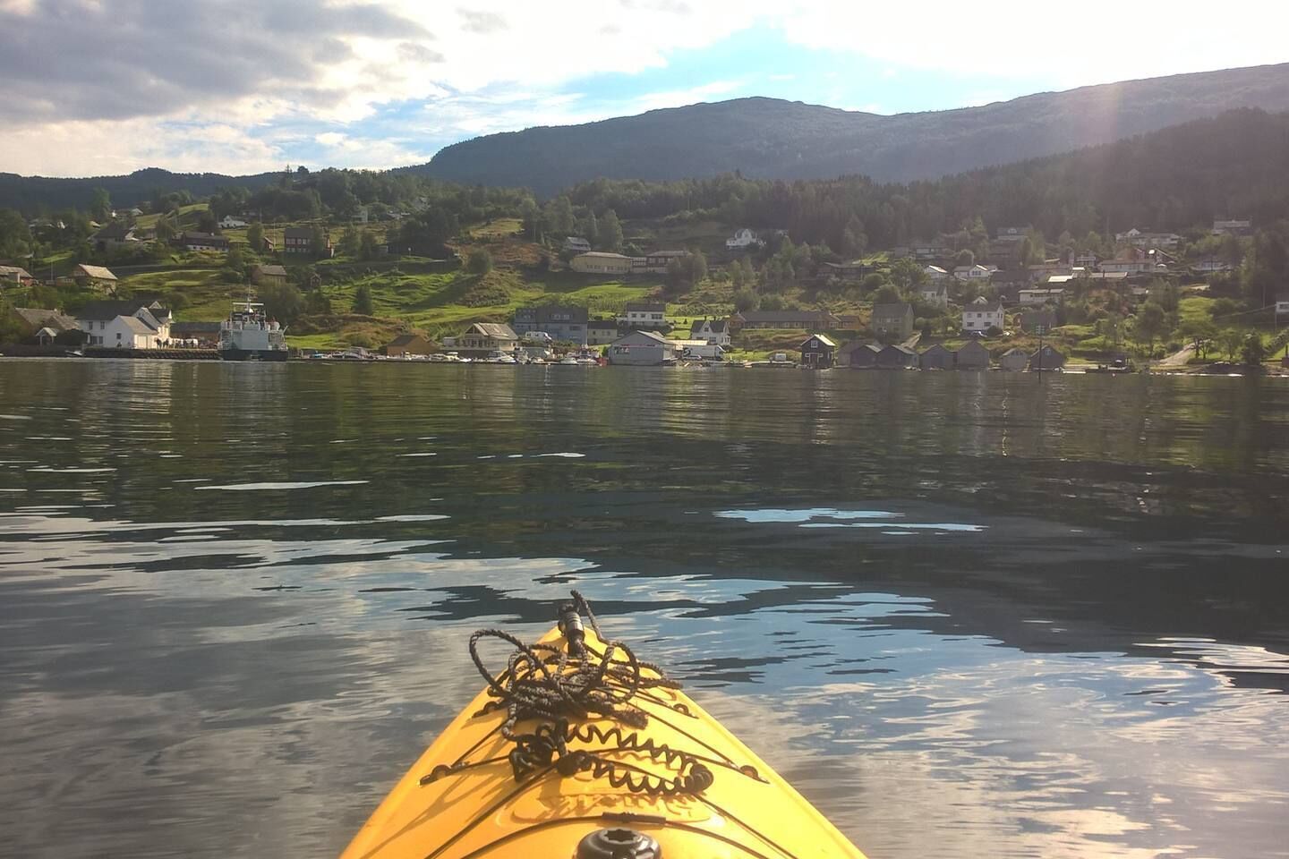 Un kayak sobre aguas tranquilas, con un pueblo y montañas al fondo.