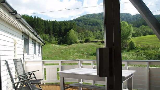 Eine Holzterrasse mit einem weißen Tisch und Stühlen, mit Blick auf eine grüne Landschaft mit Bäumen und Hügeln.