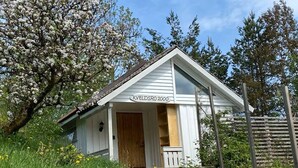 A small white building with a wooden door and steps leading up to it, surrounded by greenery and trees. - Kveldsro cabin in nice surroundings (Mosby)