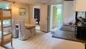 A room with a wooden ladder, a covered dining table, and chairs, a kitchen area with a sink and stove, and a door leading outside. - Kveldsro cabin in nice surroundings (Mosby)