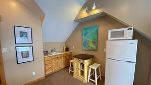 A small kitchen with wooden cabinets, a white refrigerator, a microwave, and a sink. There are two framed pictures on the wall and a colorful abstract painting above the cabinets. - Quiet location in "Swiss community" near Park City (midway)