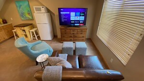 A living room with a brown leather sofa, a blue armchair, a flat-screen TV, a wooden cabinet, and a window with blinds. - Quiet location in "Swiss community" near Park City (midway)