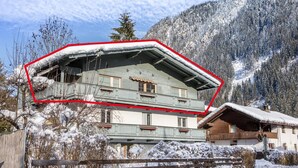 Un chalet à deux étages doté d’un balcon, entouré d’arbres et de montagnes couverts de neige.