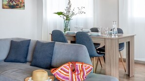 A modern living room with a grey sofa, a dining table with chairs, a vase with flowers, and a painting on the wall. - Thisean Modern Suites by Athens Stay (Kallithea)
