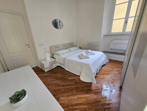Un dormitorio con cama, mesitas de noche, un radiador y una ventana.