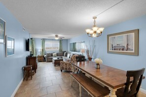 A spacious living room with a large wooden dining table, a sofa set, and a television.