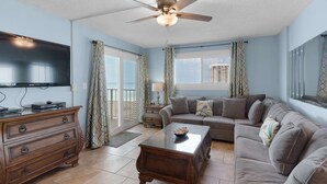 A living room with a sofa, coffee table, TV, wooden dresser, and a ceiling fan. - Regency Towers 703 (Panama City Beach)