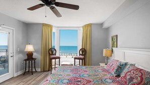 Ein Schlafzimmer mit einem großen Bett, zwei Stühlen, einem Deckenventilator, Blick auf den Ozean und einem Balkon.
