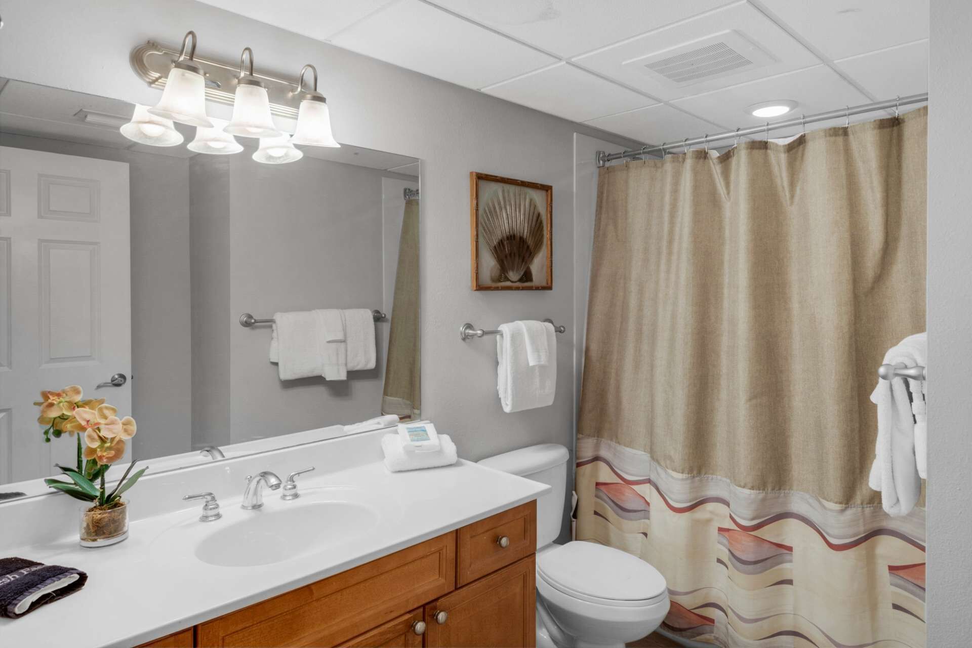 Un baño con lavamanos blanco, espejo, inodoro y cortina de ducha.