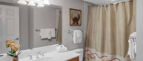 Un baño con lavamanos blanco, espejo, inodoro y cortina de ducha.