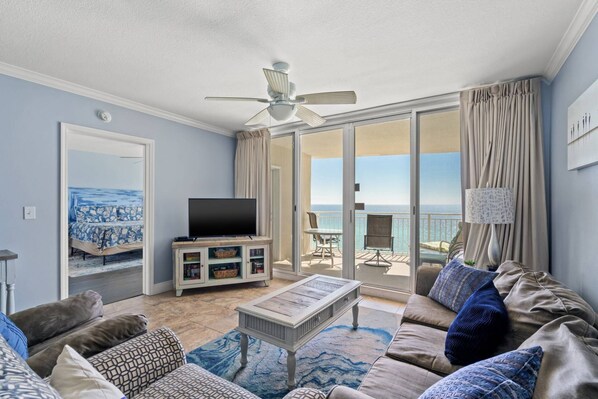 A living room with a television, sofa, and a balcony with a view. - Emerald Beach Resort by iTrip Panama City Beach (Panama City Beach)