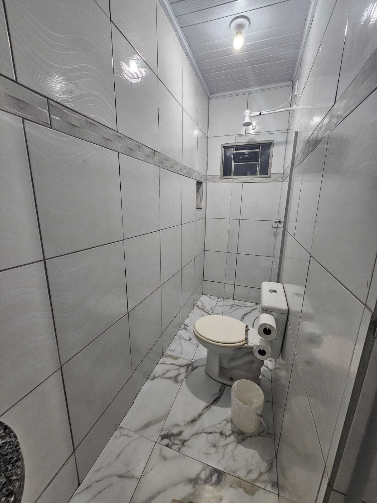 A small, tiled bathroom with a toilet, a hand dryer, and a trash bin.