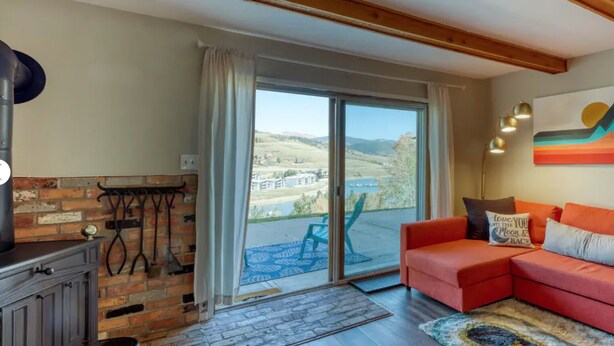 A living room with a red sofa, a fireplace, a view of a lake, and a painting on the wall. - Stunning Lake Dillon and Keystone Views from a Cozy Mountain Retreat (Dillon)