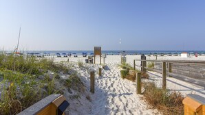 A sandy beach with wooden pathways leading to the water, umbrellas, and beach chairs. - The Enclave 203 | Gulf Front Gem | Incredible Views from Private Balcony | My Beach Getaways (Orange Beach)