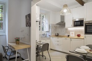 A compact kitchen with white cabinets, a microwave, an oven, a hanging light fixture, and a dining area with a table and chairs. - Cozy Holiday Home in Camogli by Wonderful Italy (Camogli)