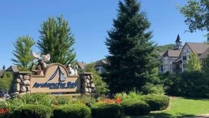 A sign with a logo and text, surrounded by greenery and a building in the background.