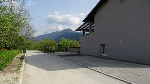 A paved driveway leading to a building with a metal gate and a mountain in the background. - Hiša Kramer - Apartment Sedlo (Kobarid)