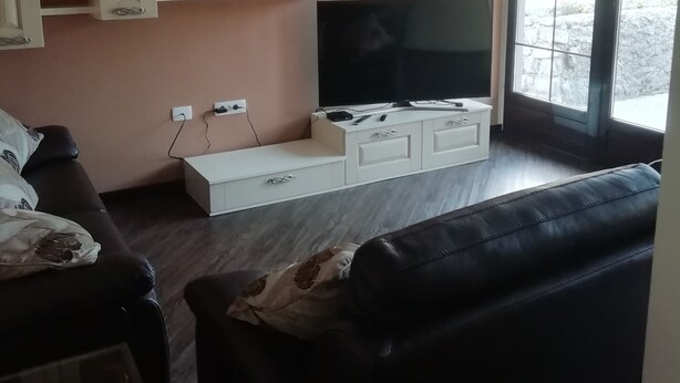 A living room with a TV, sofa, and a clock on the wall. - Hiša Kramer - Apartment Sedlo (Kobarid)