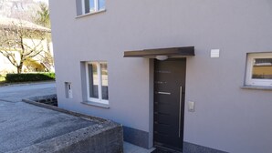 A modern building with a grey facade, a black door, and a small window to the left. - Hiša Kramer - Apartment Sedlo (Kobarid)
