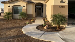 A residential building with a beige exterior, a garage door, and a landscaped front yard with small palm trees and a concrete pathway. - Area 51 Annex - Alien Lake Escape -  - Minutes from the River / Casinos / Lake! (Bullhead City)