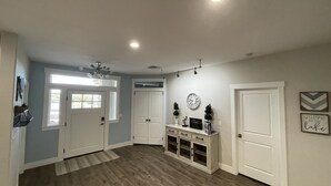 A spacious hallway with wooden flooring, white doors, and a ceiling fan. There is a small cabinet with decorative items and a clock on the wall. - Area 51 Annex - Alien Lake Escape -  - Minutes from the River / Casinos / Lake! (Bullhead City)