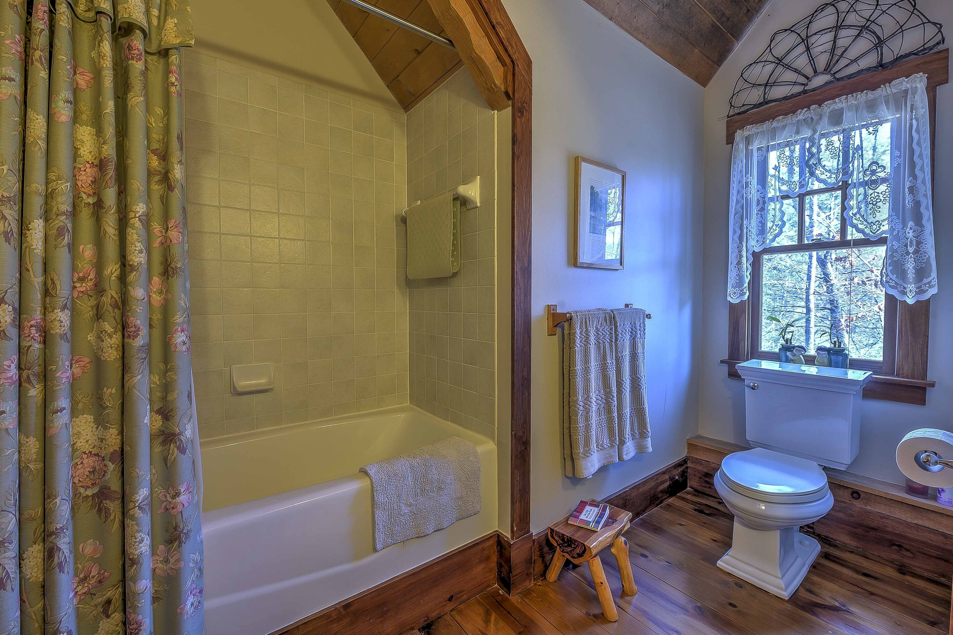 Une salle de bain avec douche, toilettes et fenêtre avec rideaux.