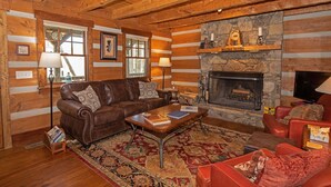 A log cabin interior with a fireplace, leather sofas, a coffee table, and a stone wall.