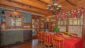 A wooden cabin interior with a kitchen, dining area, and a large window with blinds.