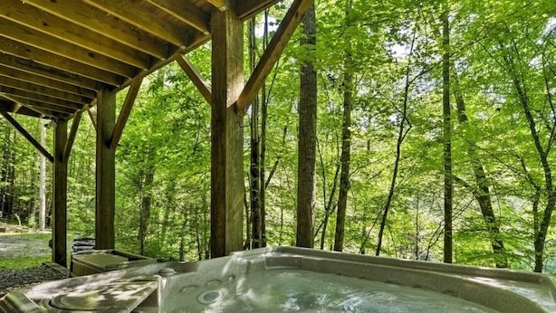 A hot tub under a wooden pergola surrounded by a forest.