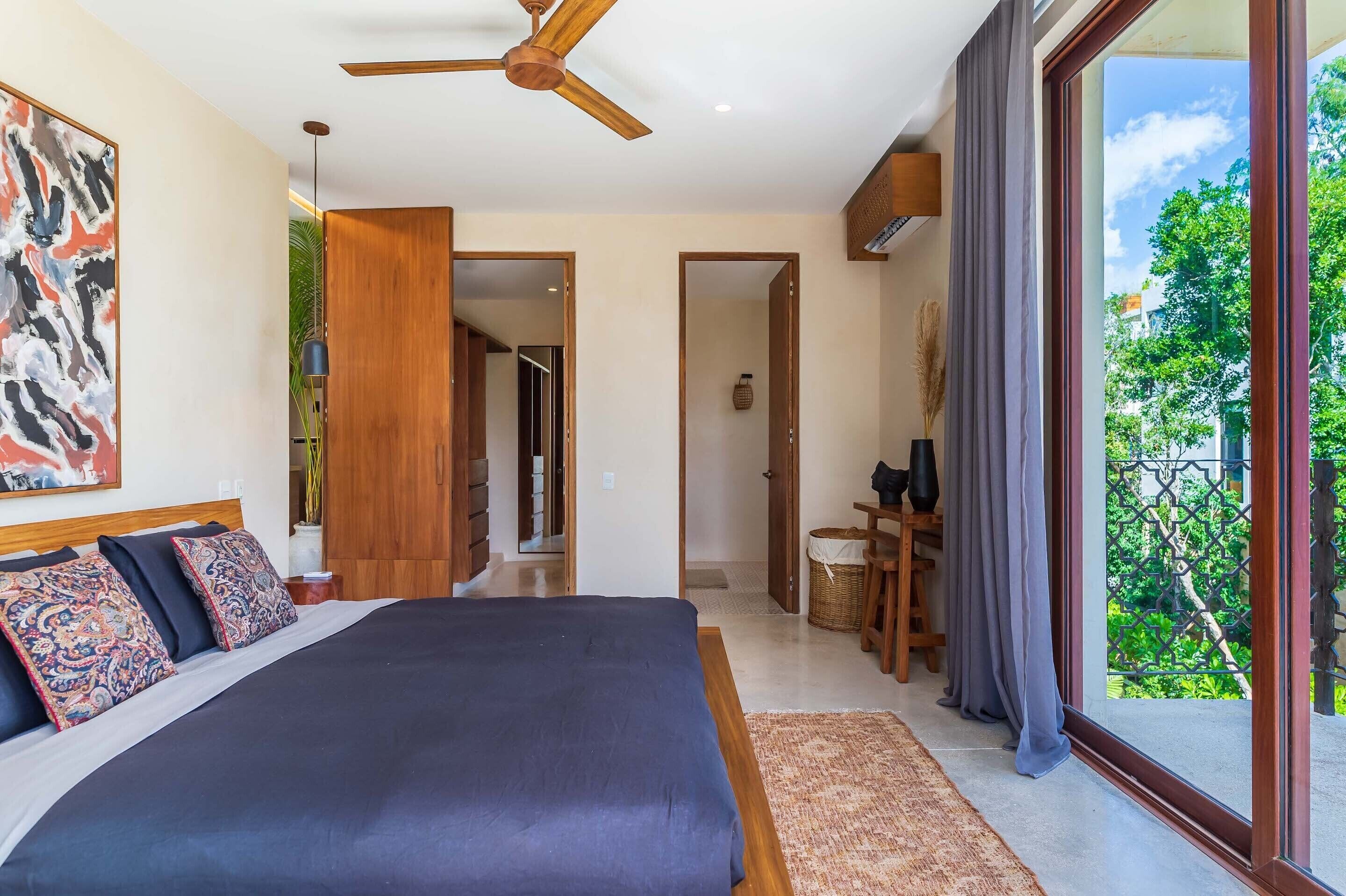 Une chambre moderne avec un grand lit, un ventilateur de plafond et une vue sur la verdure environnante.