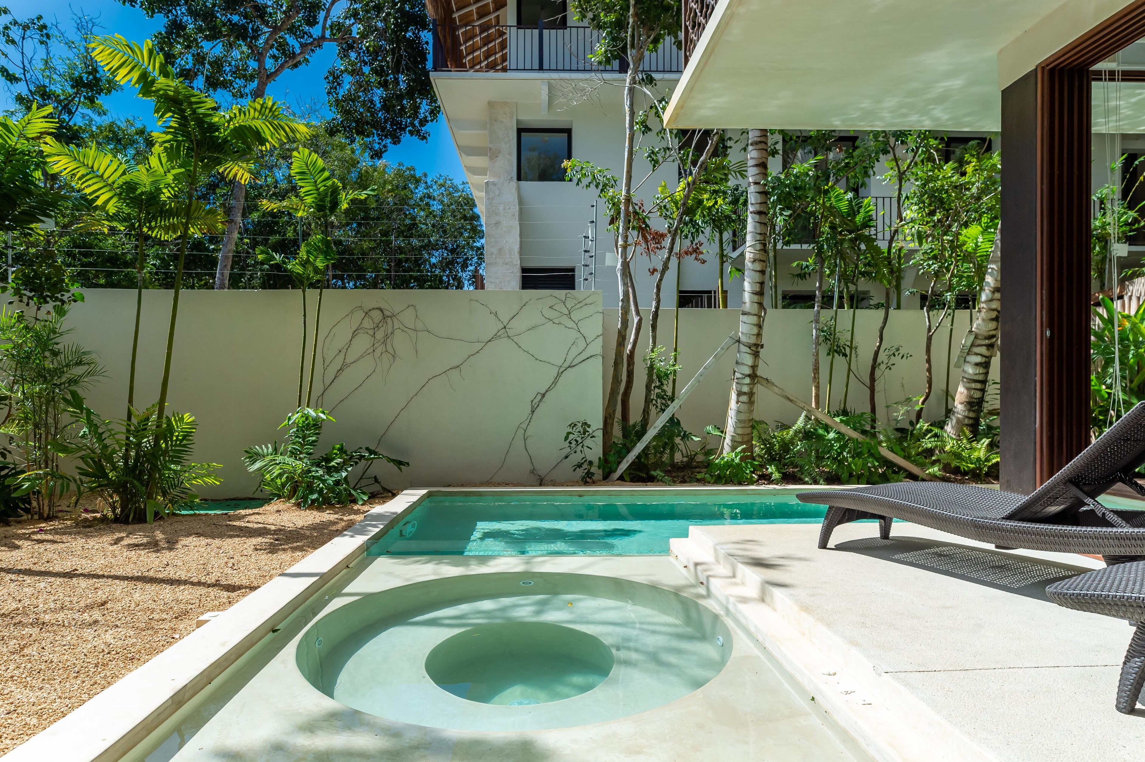 A swimming pool with lounge chairs, surrounded by greenery and a modern building in the background.