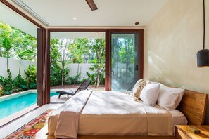 Une chambre dotée d’un grand lit, offrant une vue sur une piscine, et dont la porte-fenêtre donne sur un jardin.
