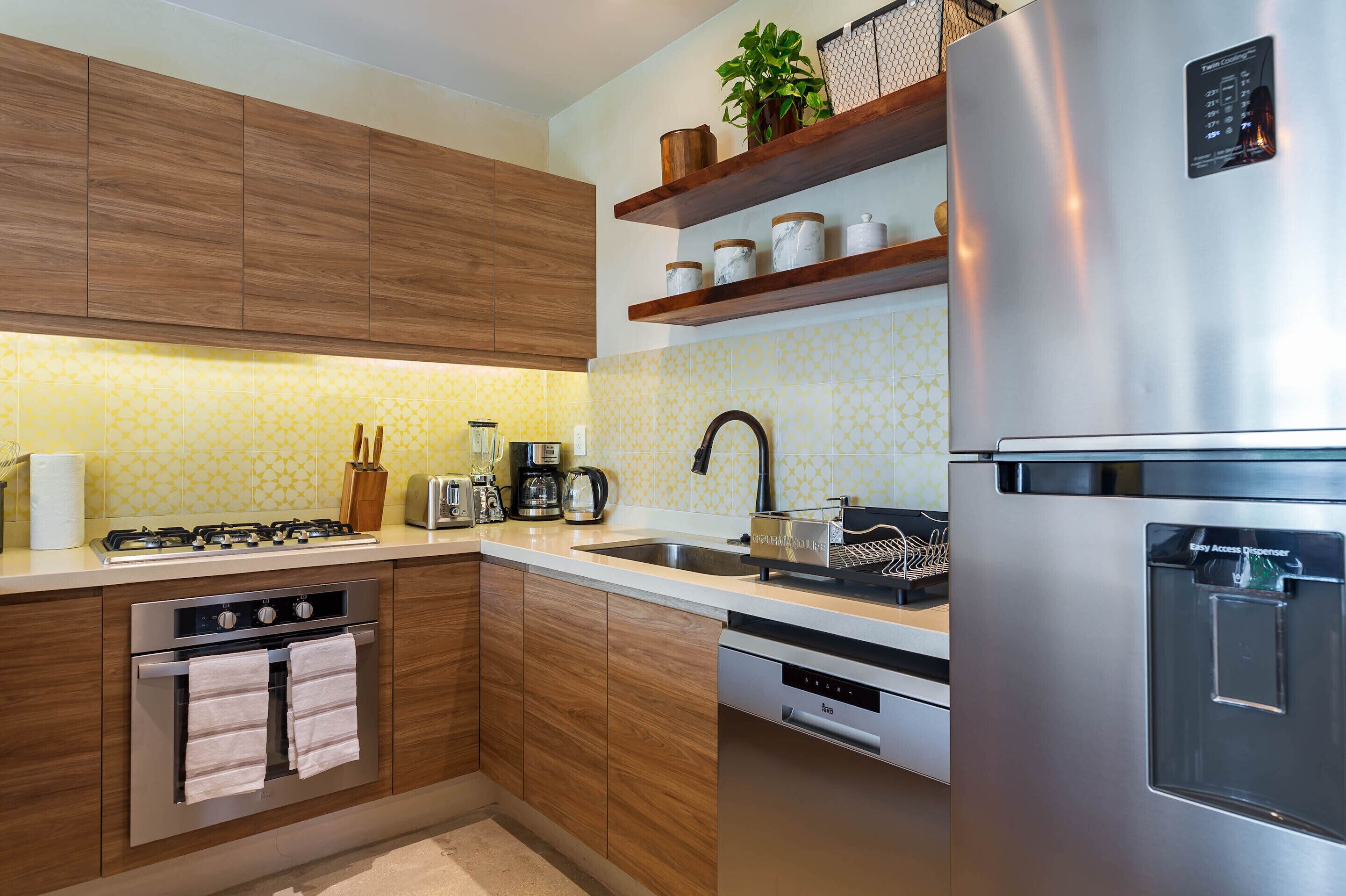 A modern kitchen with wooden cabinets, stainless steel appliances, and a yellow patterned backsplash.