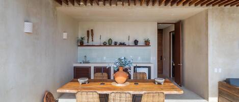 A modern kitchen with a wooden table and wicker chairs, a large vase with flowers, and a kitchen counter with various items.