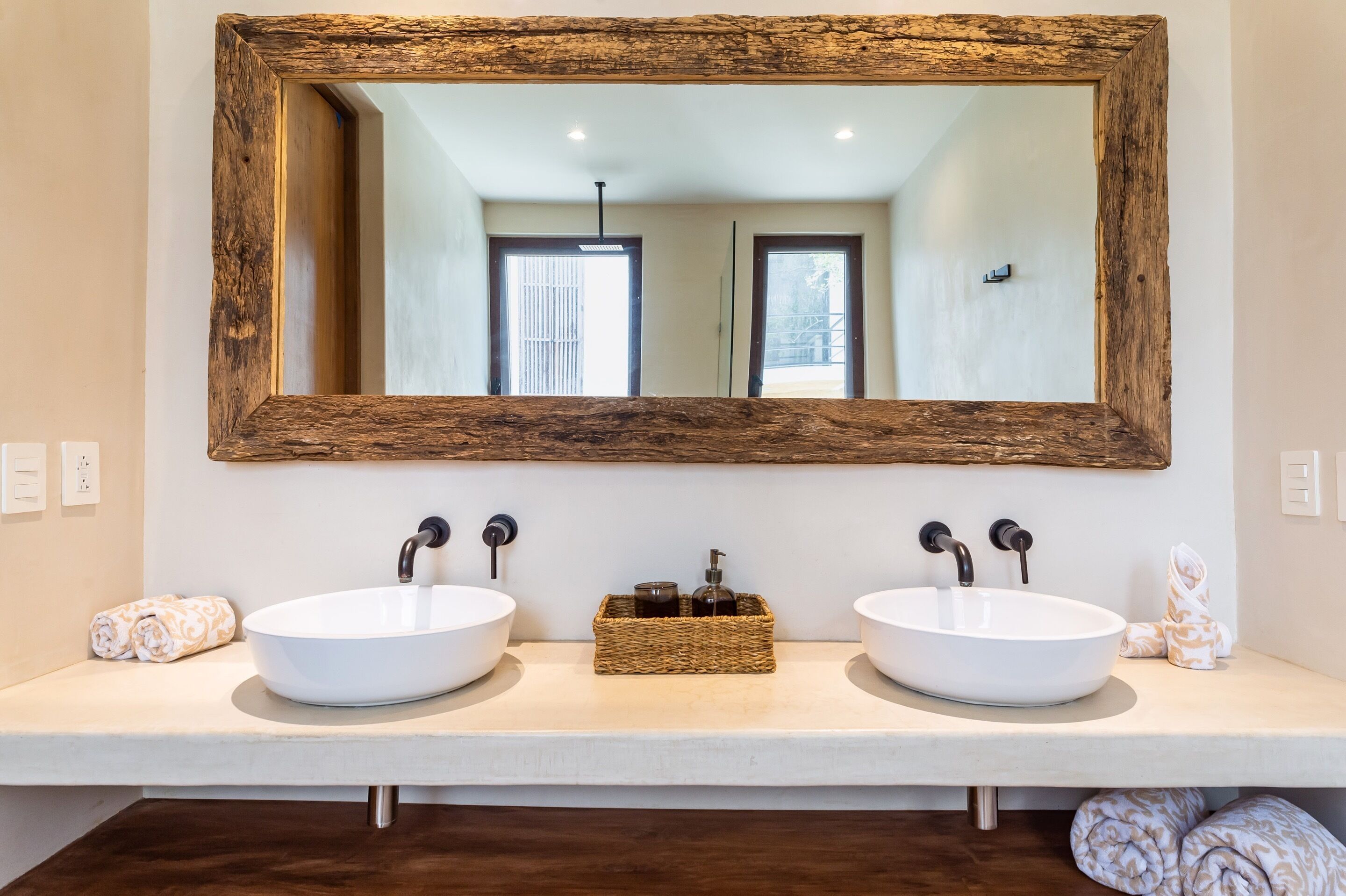 Une salle de bain avec deux lavabos blancs, un miroir à cadre en bois et un panier tressé posé sur le comptoir.