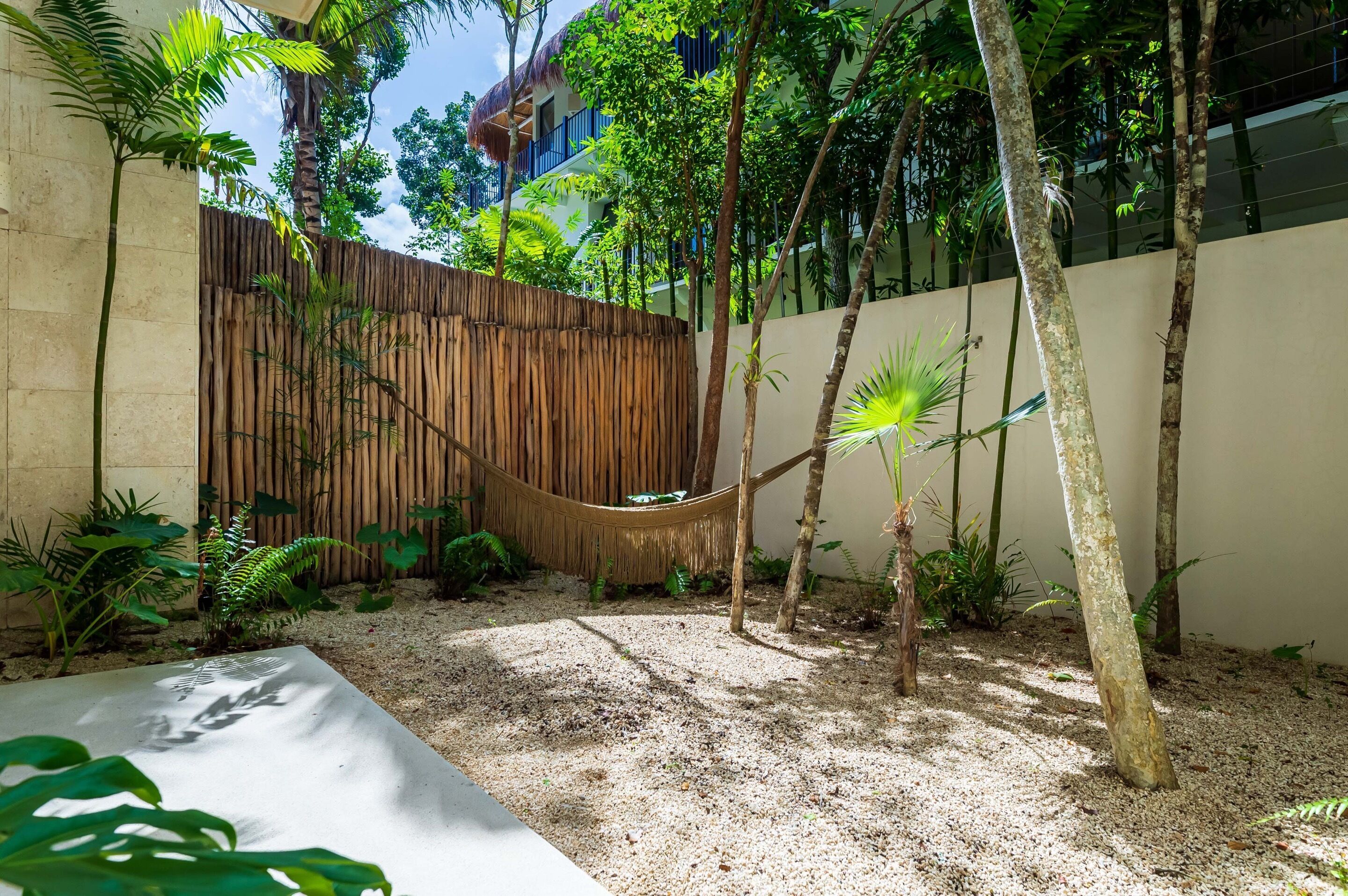 A hammock in a garden area with trees and a wooden fence.