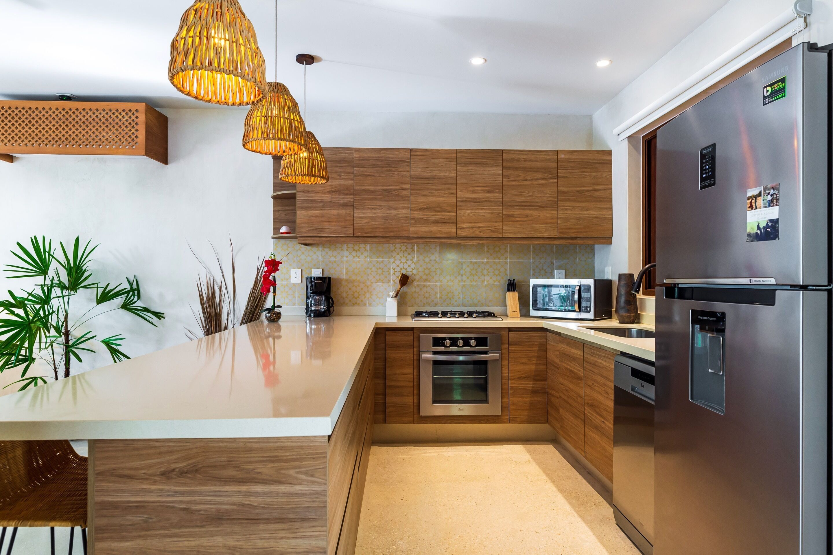 Eine moderne Küche mit Holzschränken, Edelstahlgeräten, einer großen Kochinsel und hängenden Korbschwinglampen.