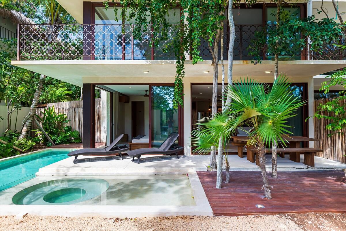 Une maison moderne à deux étages dotée d’une piscine, d’un espace salon extérieur et de plantes tropicales.