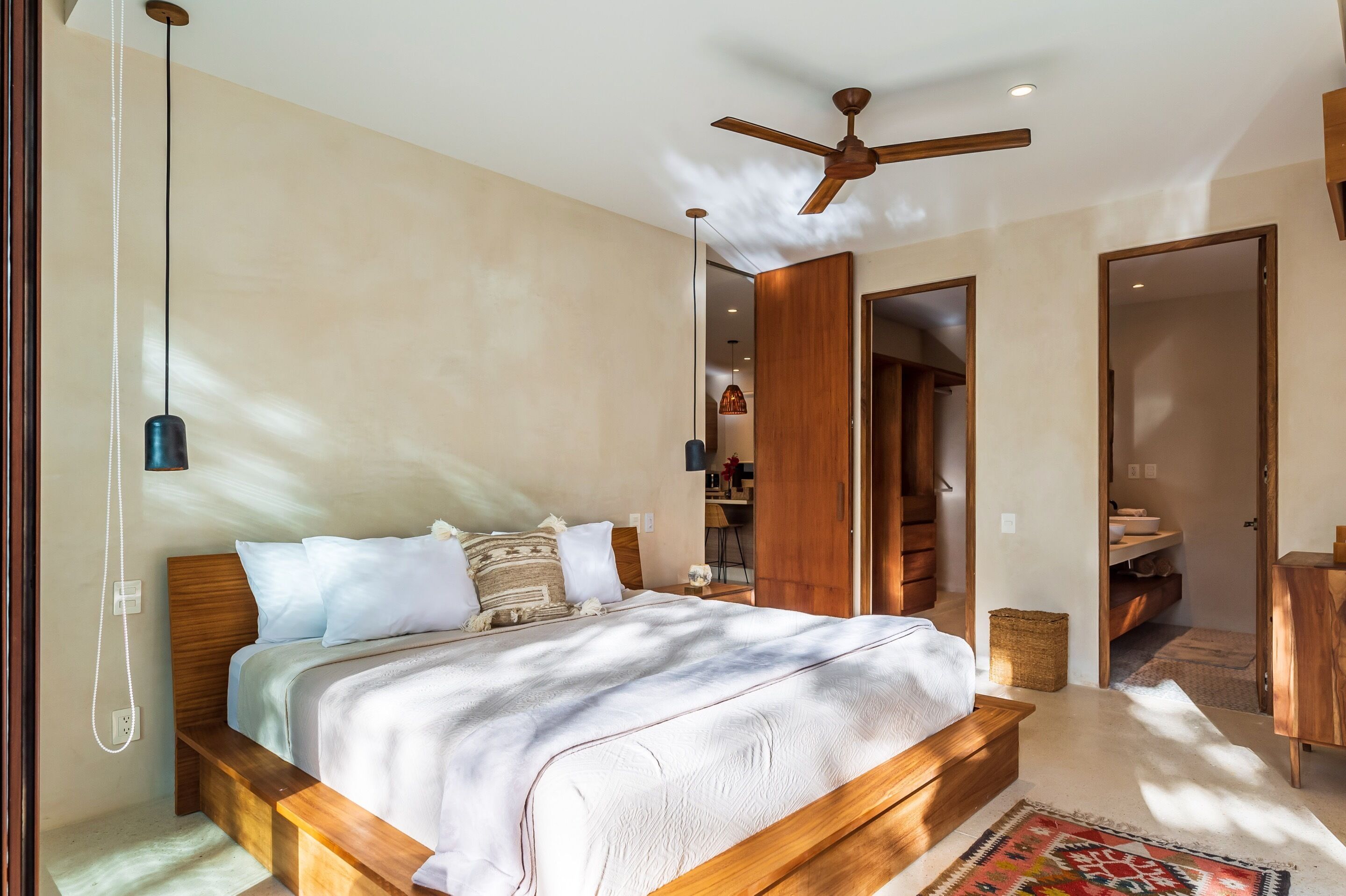Een slaapkamer met een houten bed, een plafondventilator en uitzicht op de badkamer.