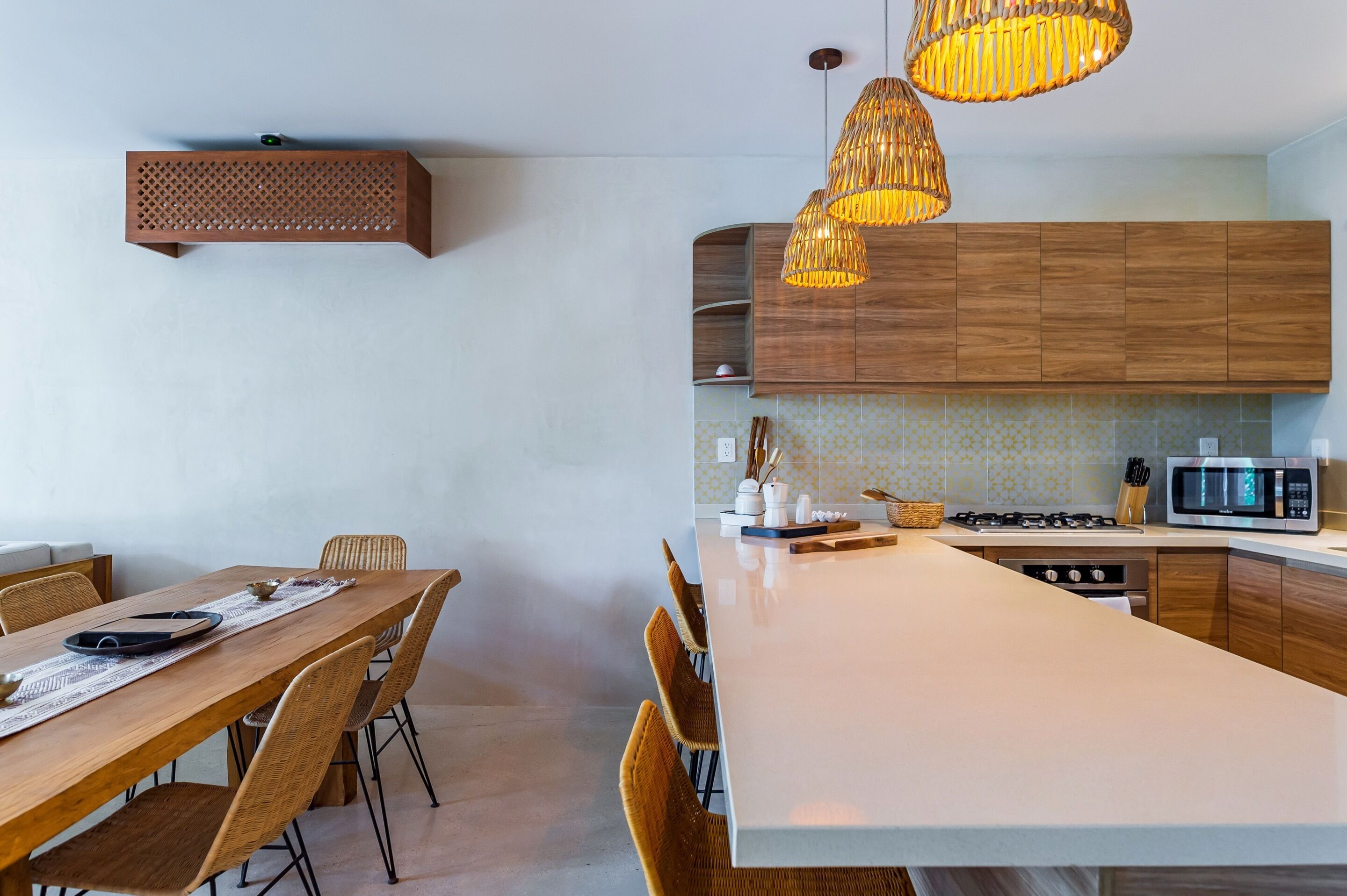 A modern kitchen with wooden cabinets, a white countertop, and a dining area with a wooden table and chairs.