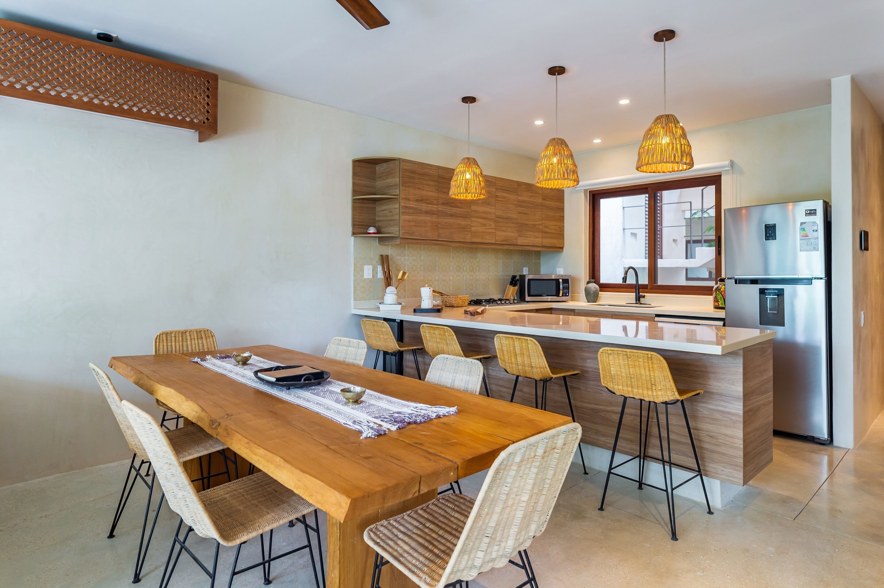 A modern kitchen with a wooden dining table, wicker chairs, and pendant lights.