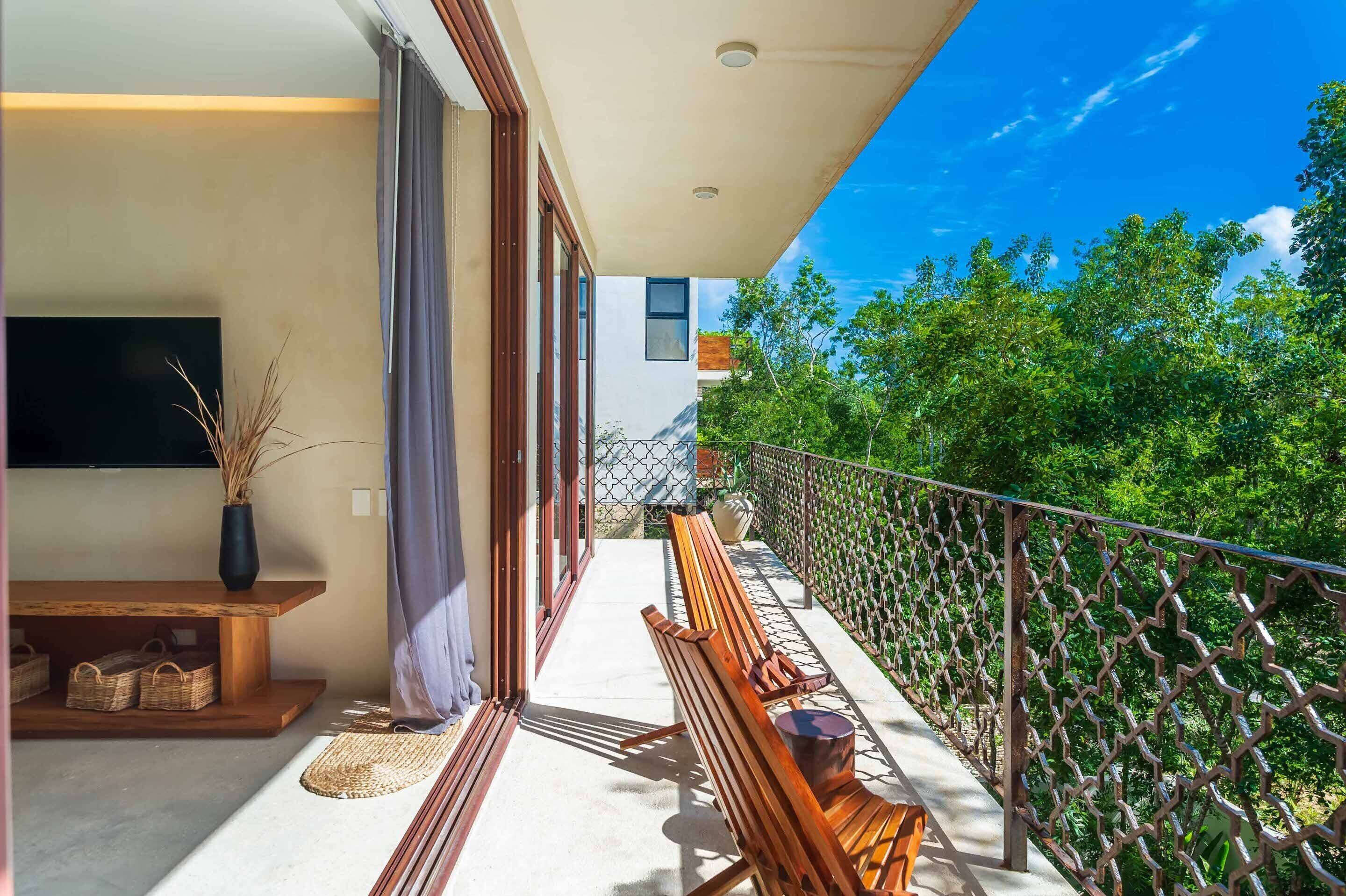 A balcony with a wooden bench, a TV, and a vase of dried plants.