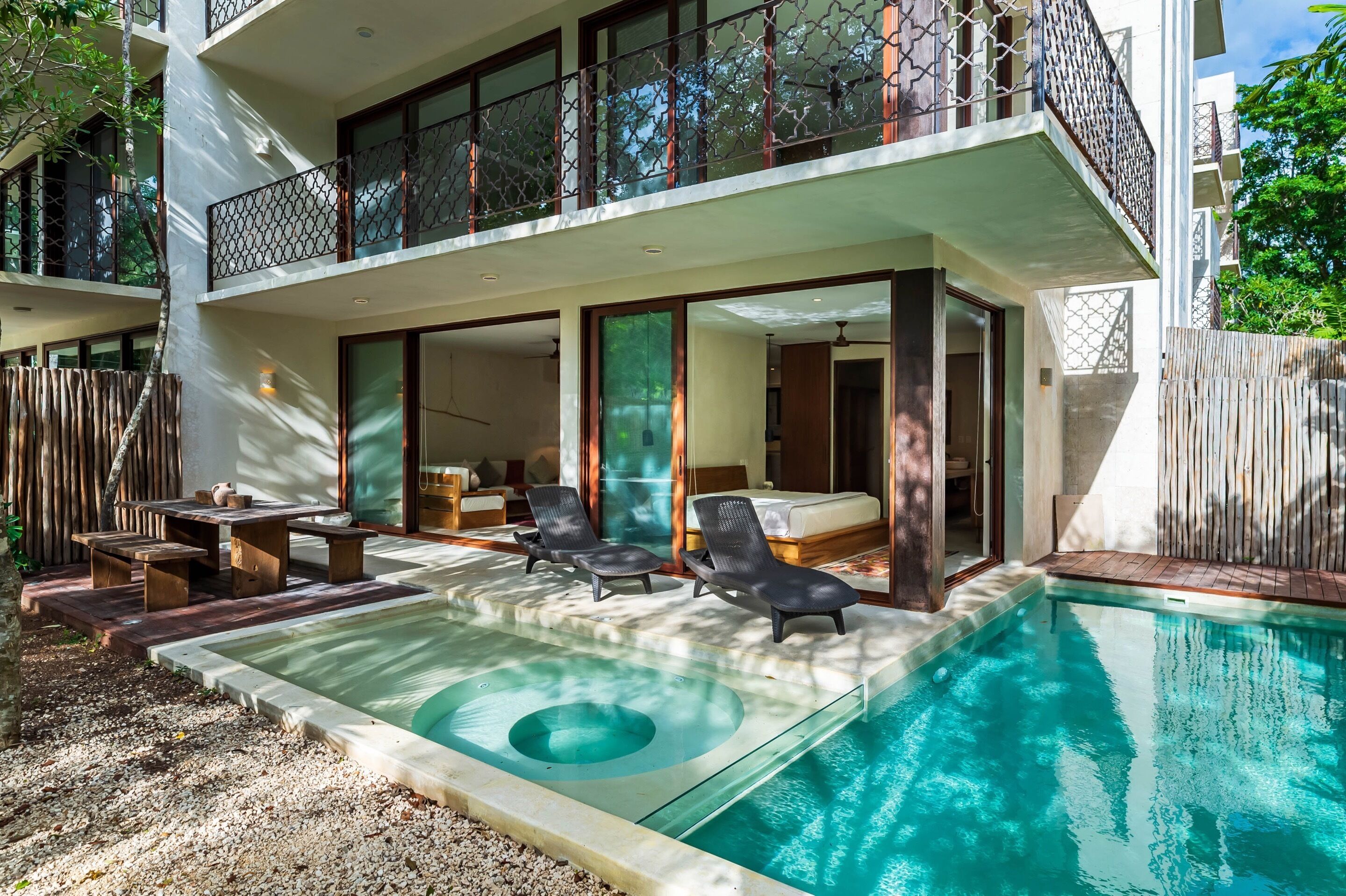 A modern two-story building with a swimming pool, outdoor seating, and a balcony with a metal railing.