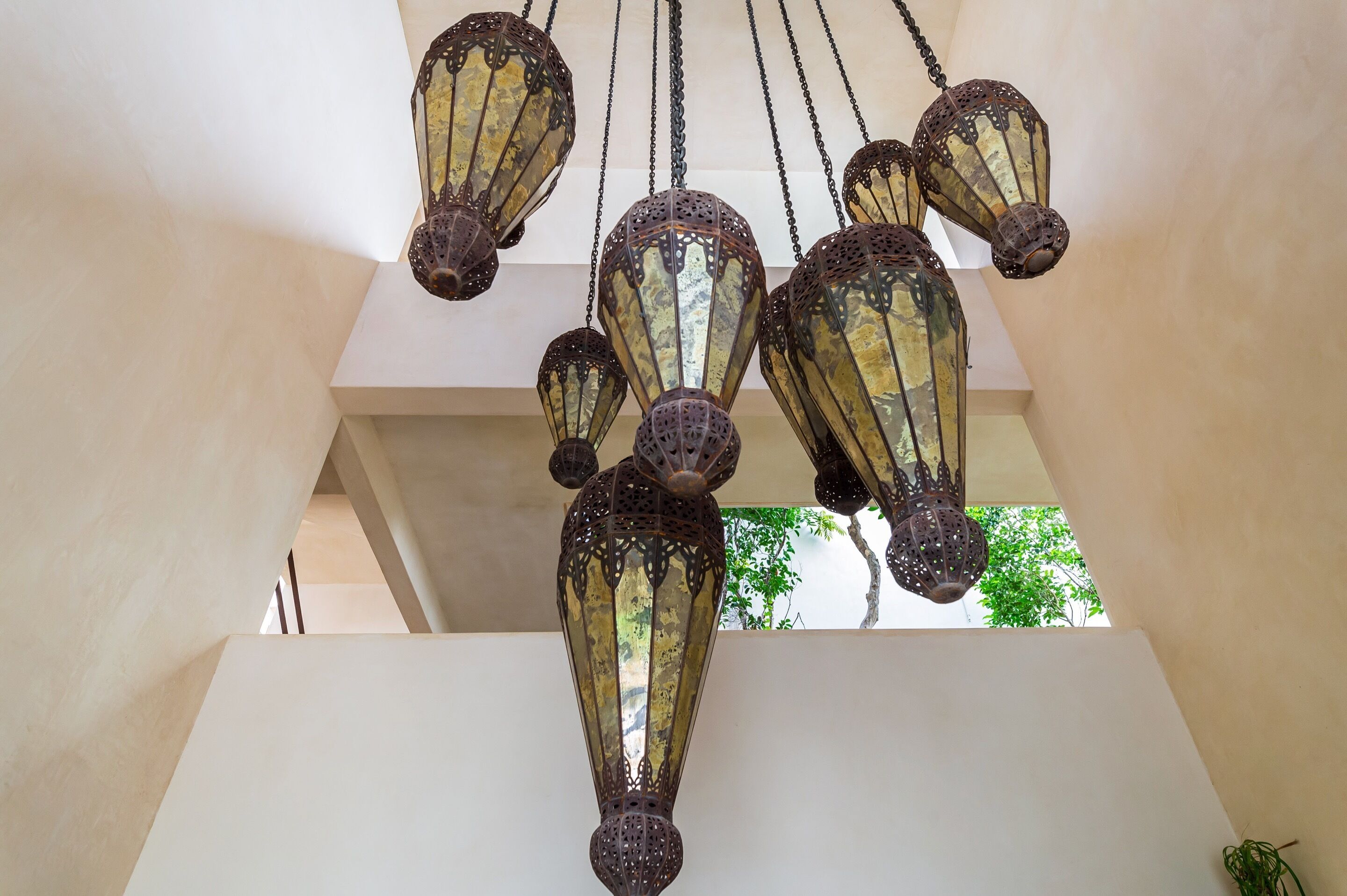 A ceiling with hanging lanterns and a view of greenery outside.