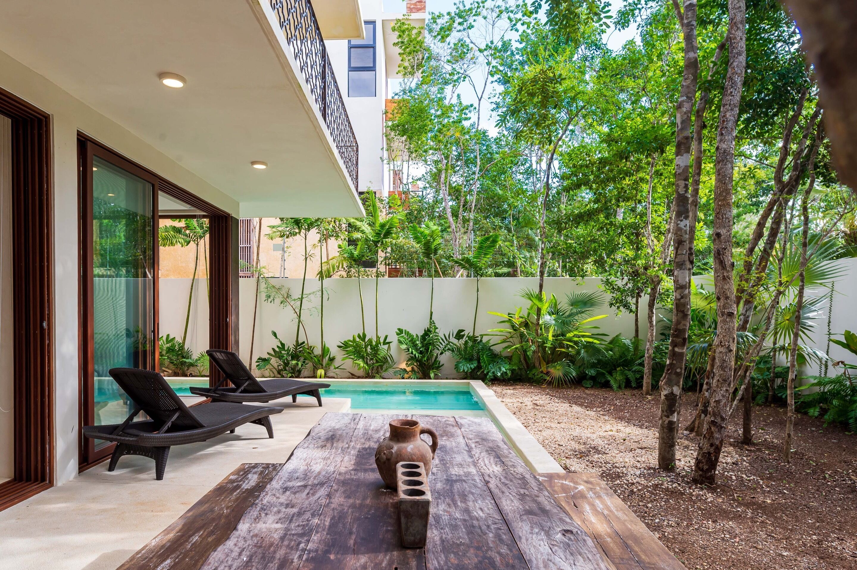 Un espacio exterior moderno con piscina, sillas de descanso y una mesa de madera rústica.