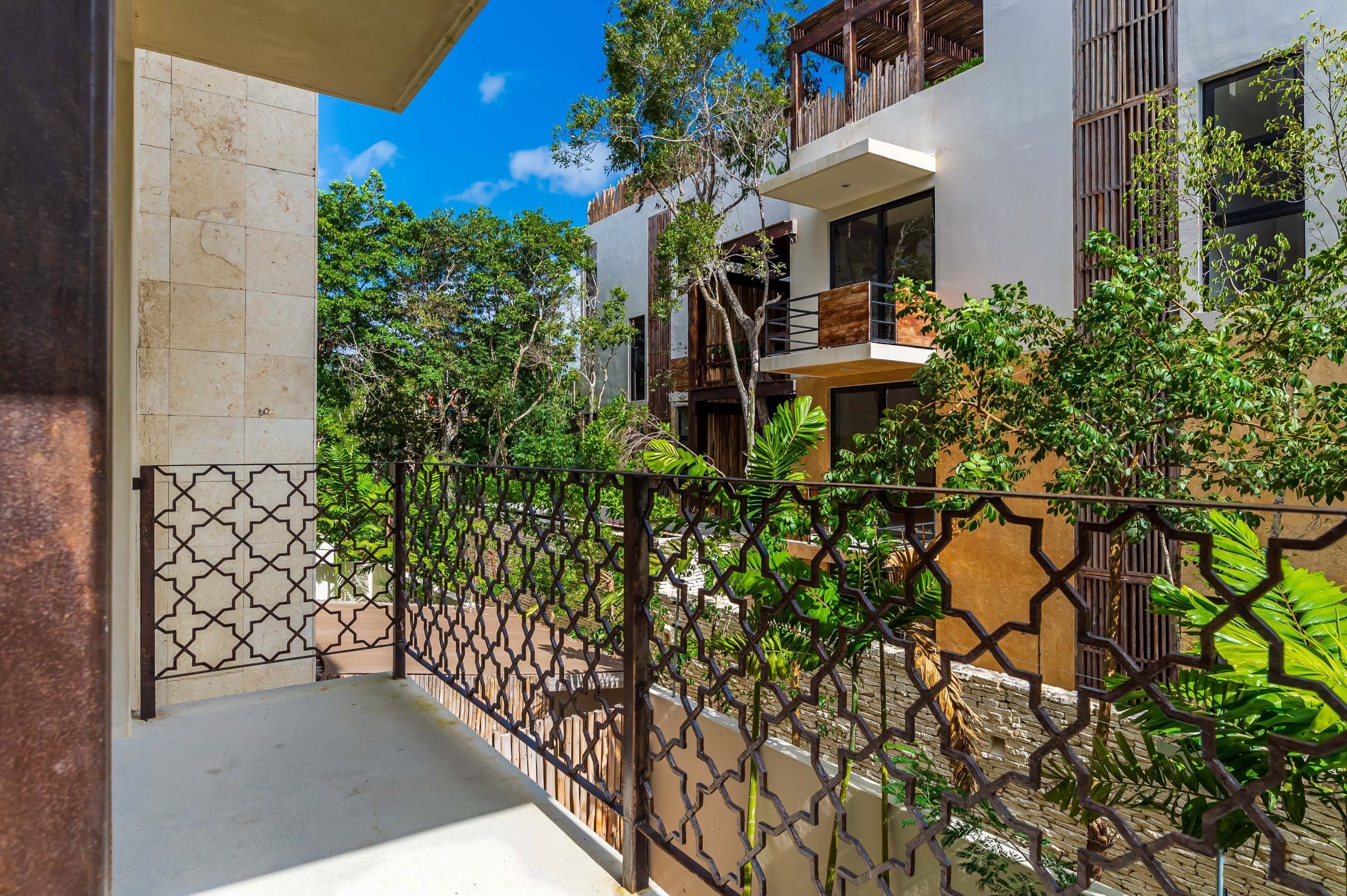 A modern building with a balcony, surrounded by lush greenery and a decorative fence.