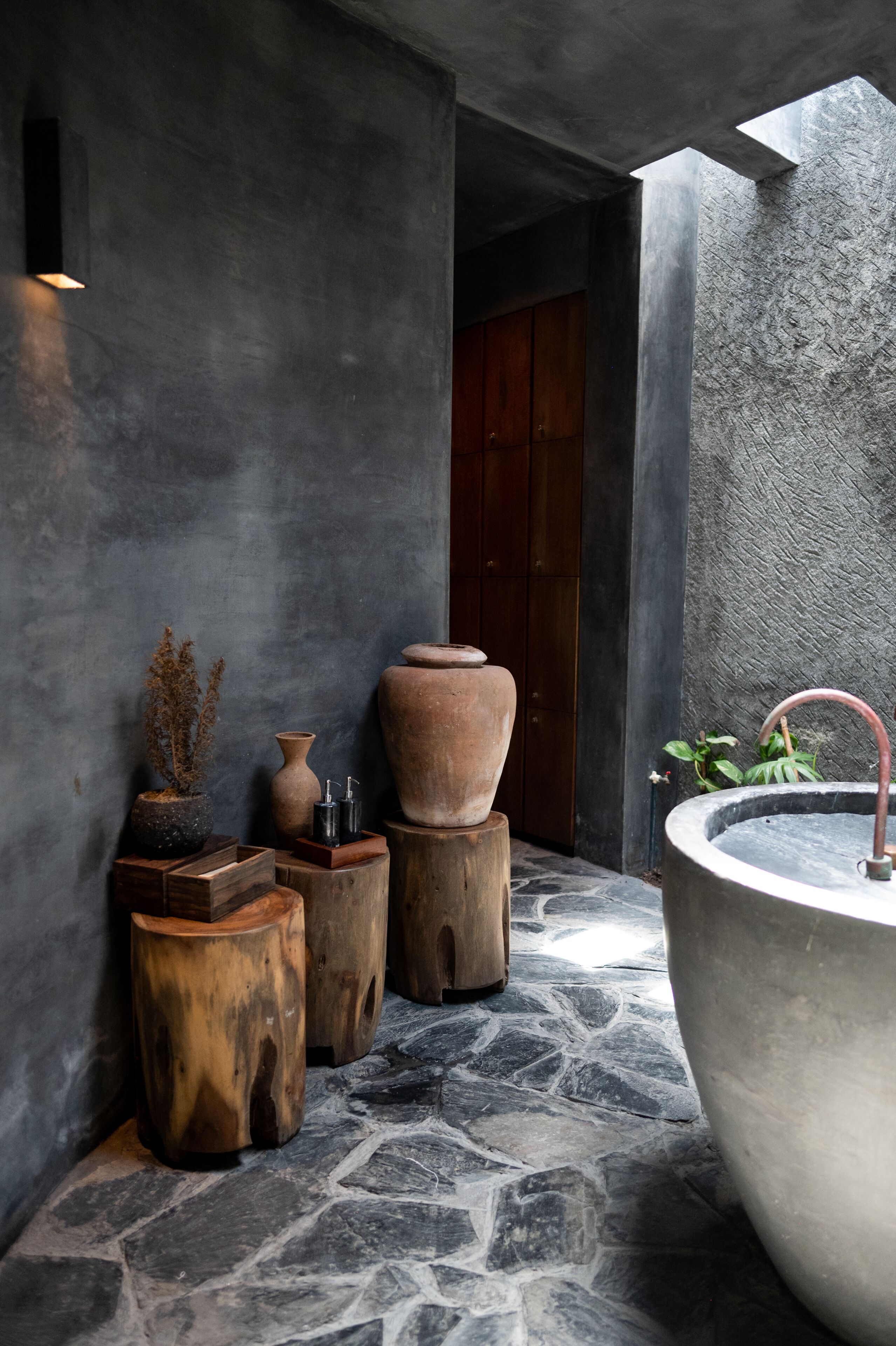 A stone-floored bathroom with a large bathtub, wooden stools, and various decorative items.